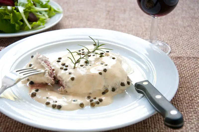 Green Peppercorn Sauce served over baked chicken on a white plate.