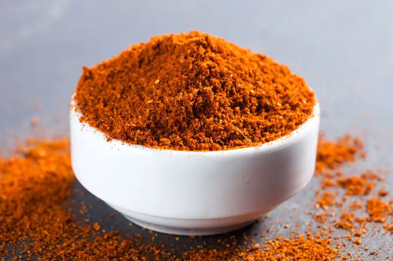 A white bowl overflowing with a brilliant, rust colored homemade shawarma spice mix.