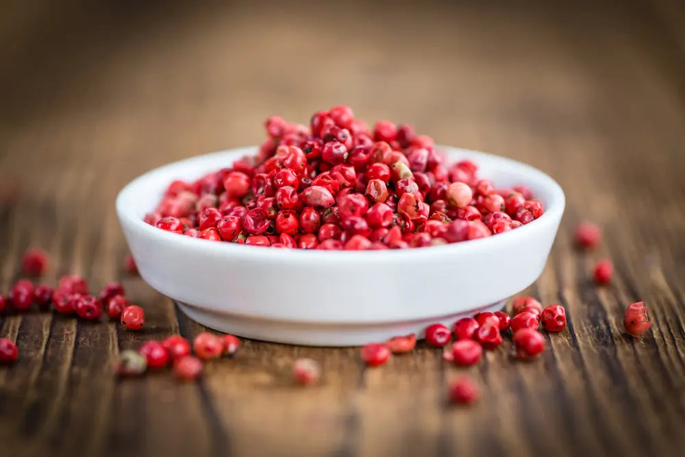 A white ceramic bowl filled with pink peppercorns