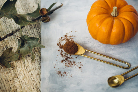 A measuring spoon full of homemade pumpkin pie spice next to a pumpkin