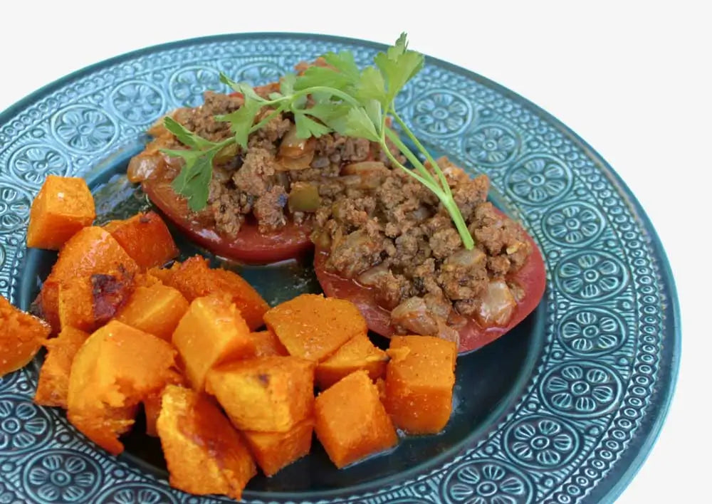 Bunless sloppy joes served on sliced tomatoes pictured on a blue plate next to ancho spiced roasted butternut squash.