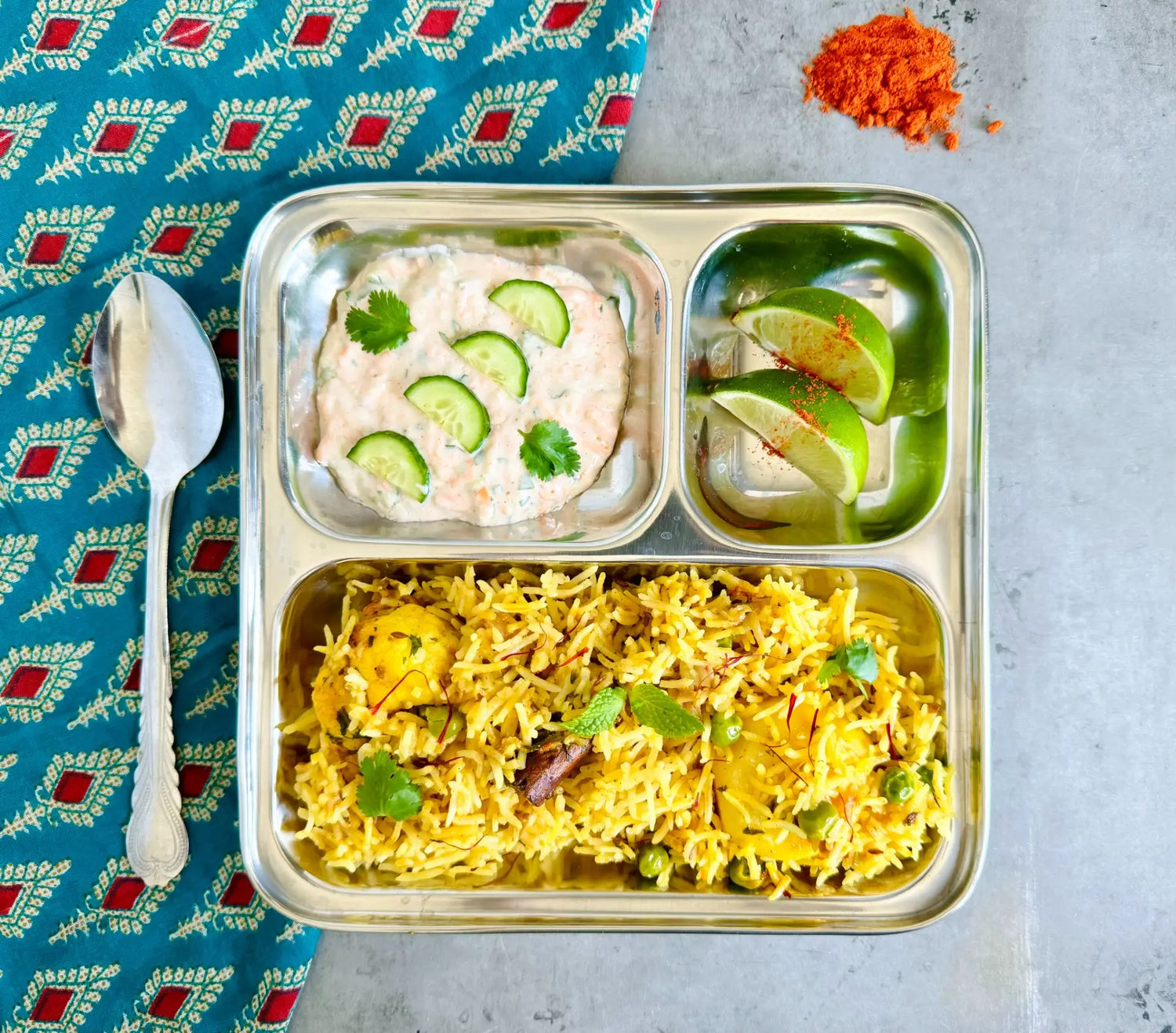 A metal dinner tray filled with vegetarian biryani and carrot raita.