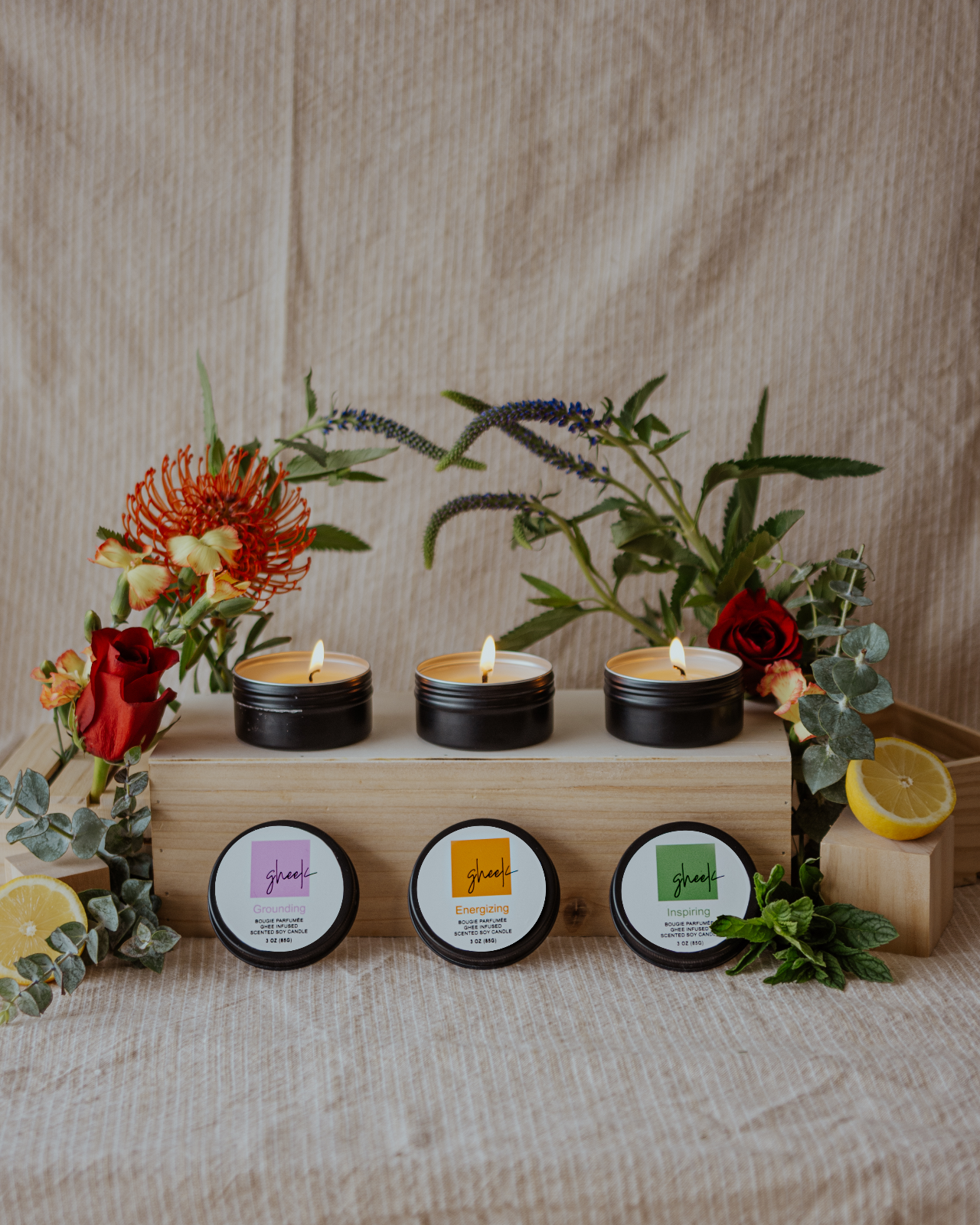 a set of ayurvedic ghee candles lit next to a display of fresh herbs, flowers, and citrus