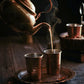 Freshly brewed Assam Orthodox tea being poured into two brass cups