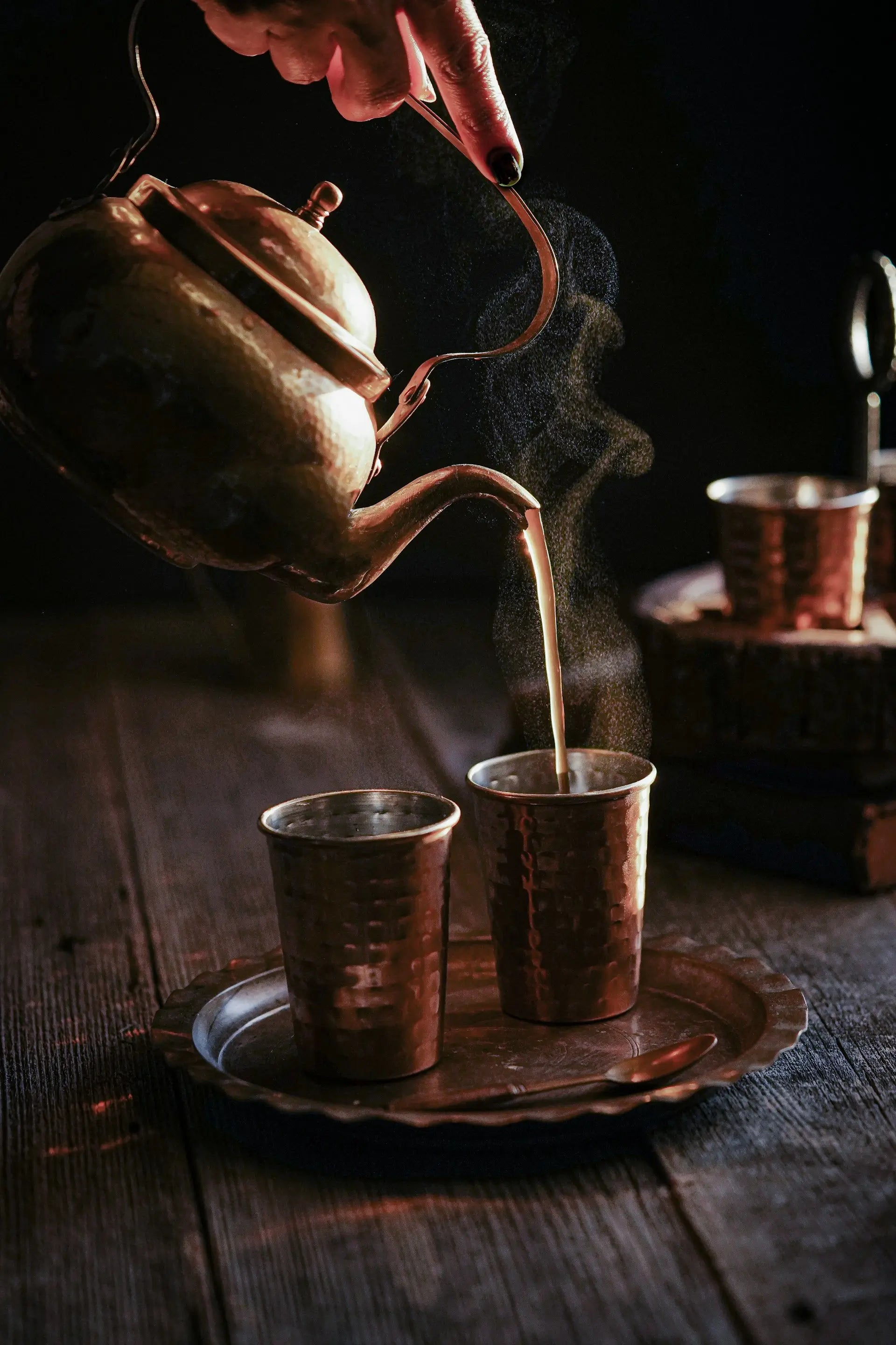 Freshly brewed Assam Orthodox tea being poured into two brass cups