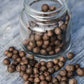 organic whole allspice berries in a glass jar and on a grey wooden background