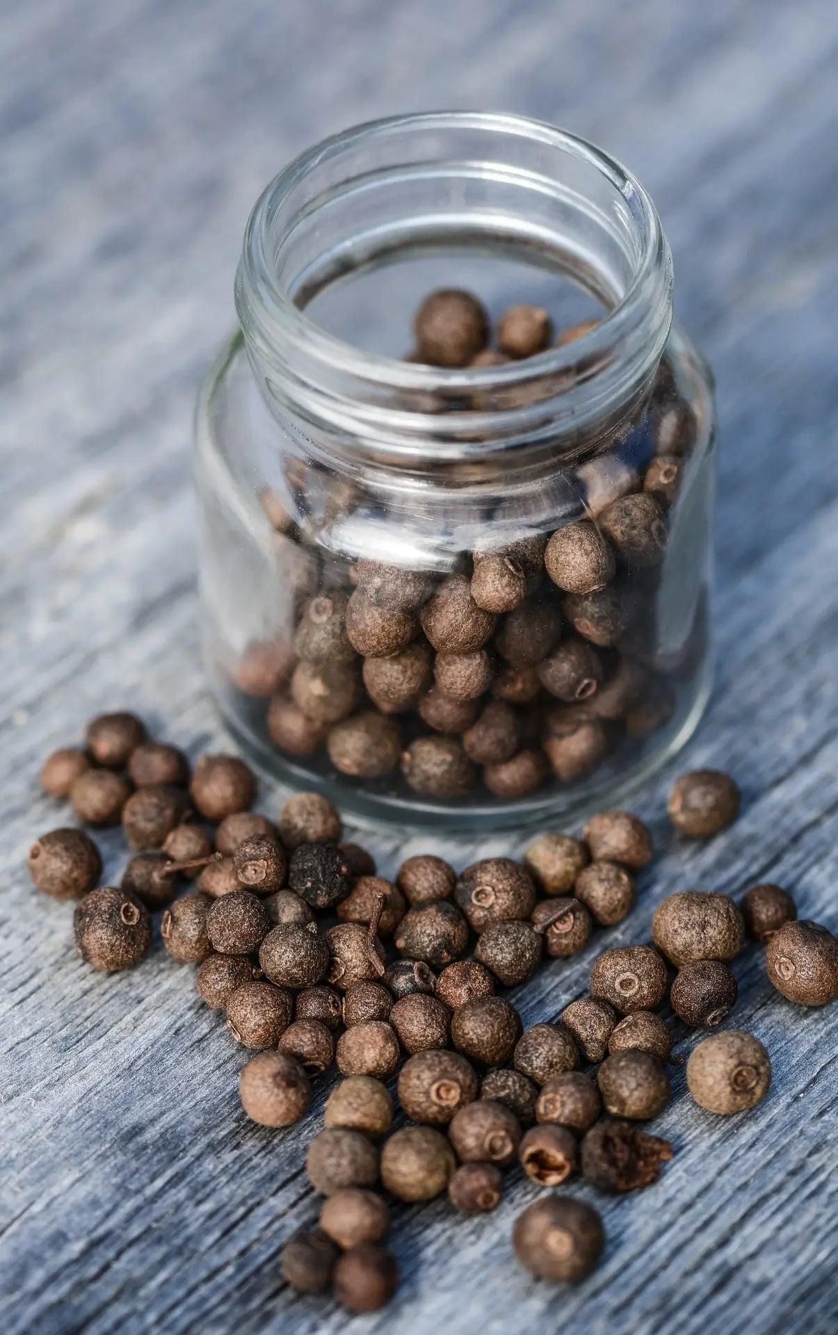 organic whole allspice berries in a glass jar and on a grey wooden background