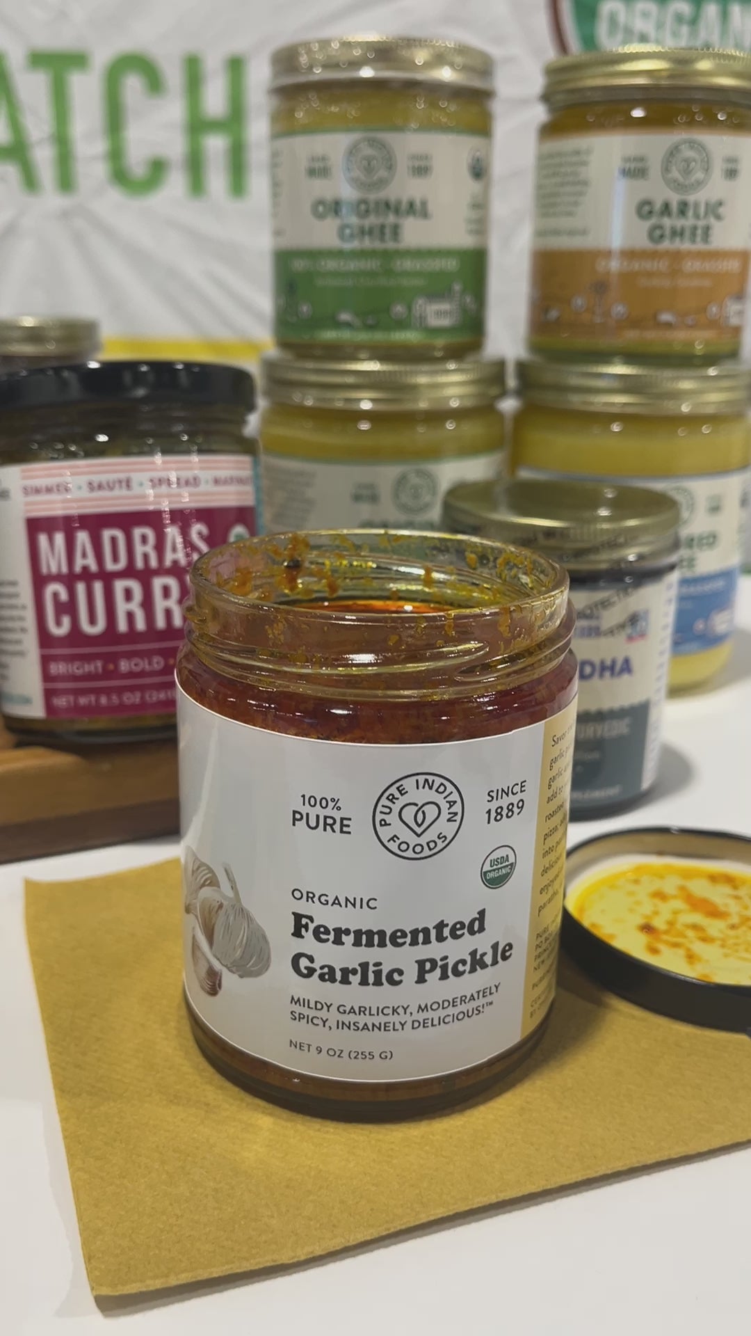 An open jar of spicy pickled garlic achaar being stirred with a wooden spoon. Then the spoon lifts and you can see the consistency of the indian garlic pickle.