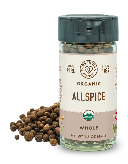 A jar of organic allspice berries from Pure Indian Foods in front of a pile of whole allspice on a white backdrop